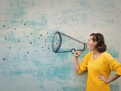 Young woman holding an imaginary megaphone and shouting into it